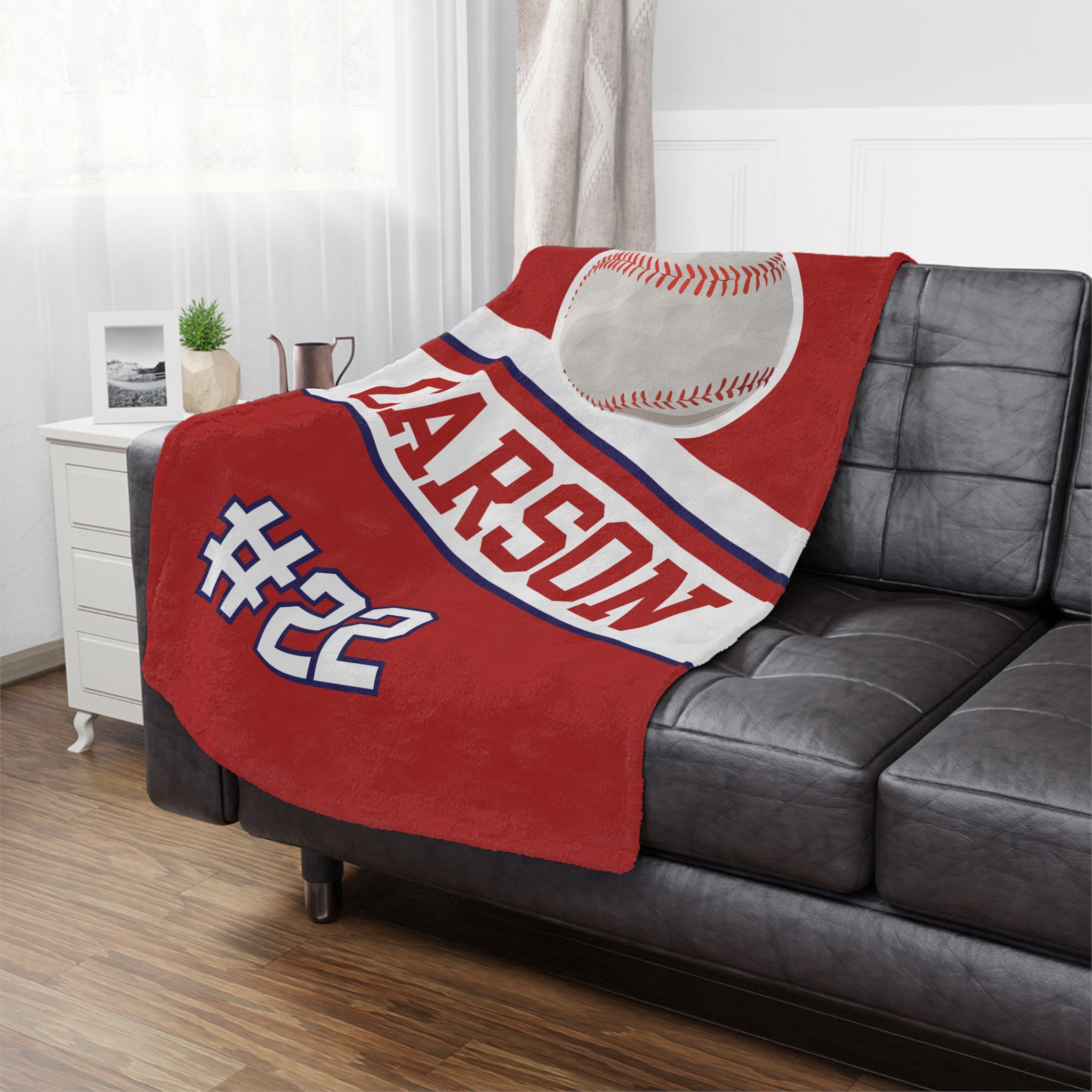 Red blanket with baseball design and text on a gray sofa in a living room.