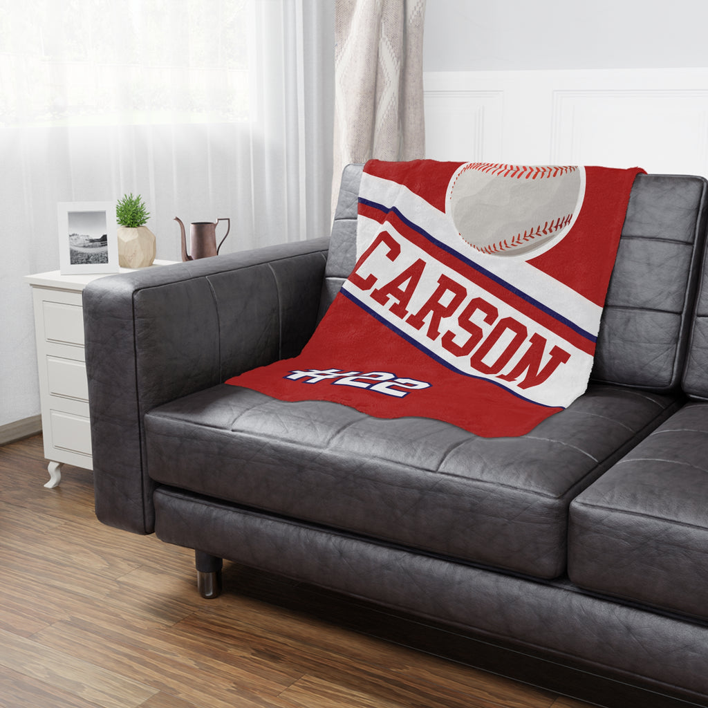 Red blanket with 'CARSON' and a baseball design on a gray sofa in a living room.