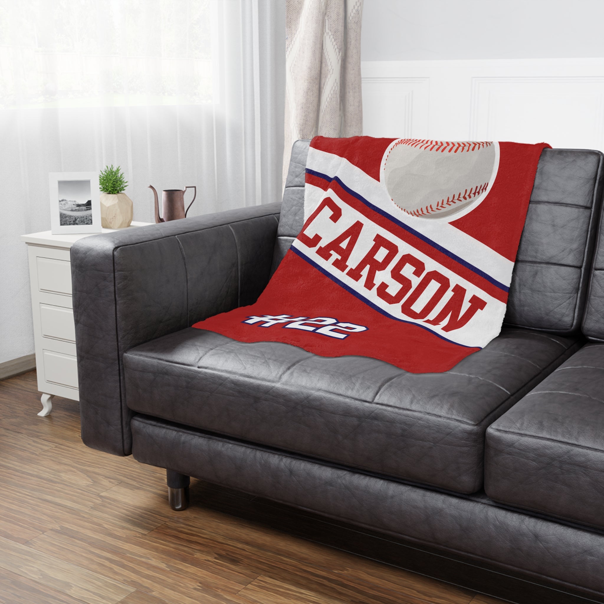 Red blanket with 'CARSON' and a baseball design on a gray sofa in a living room.