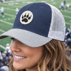 Woman wearing a blue and gray cap with a paw print logo at a sports event.