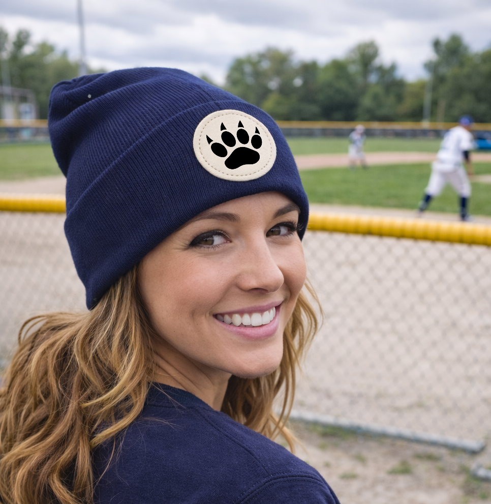 Woman wearing a navy blue beanie with a paw print design on a baseball field.