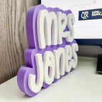 Purple and white decorative sign with 'Mrs Jones' on a desk